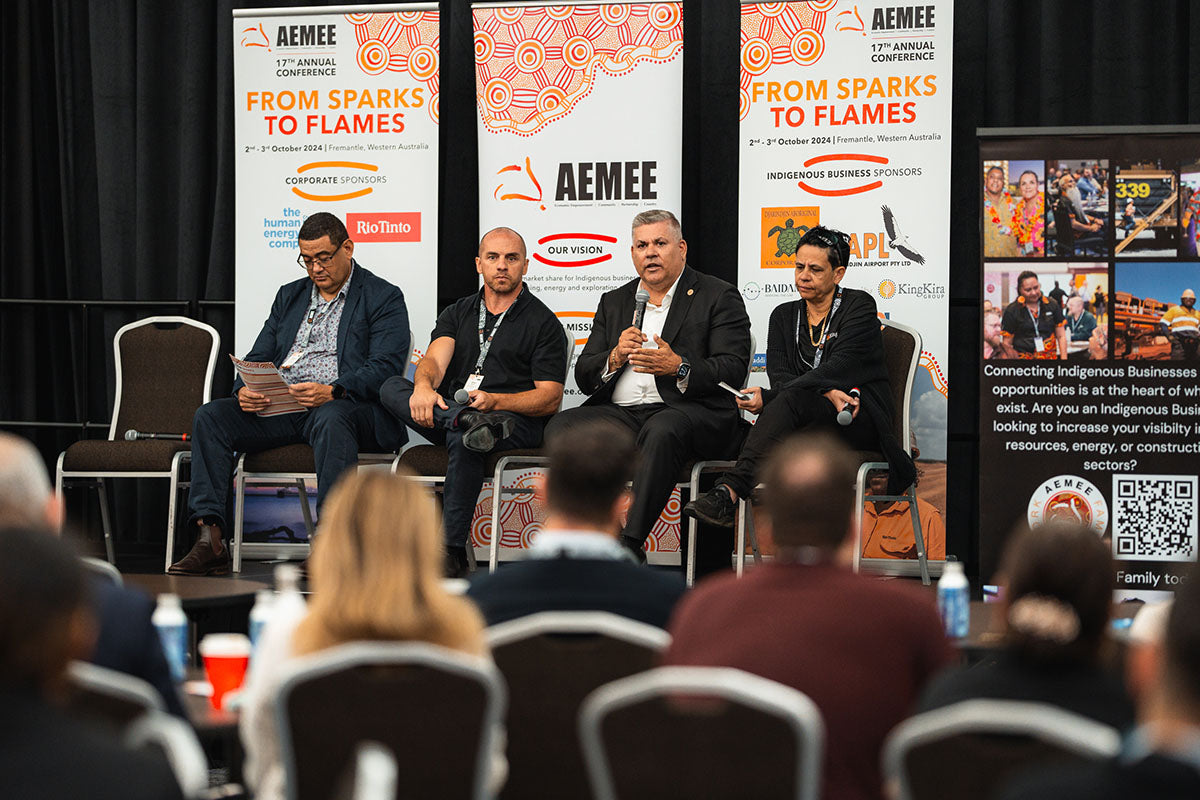 Seated corporate and community delegates watching a main-stage panel forum from their tables at the annual national AEMEE conference.