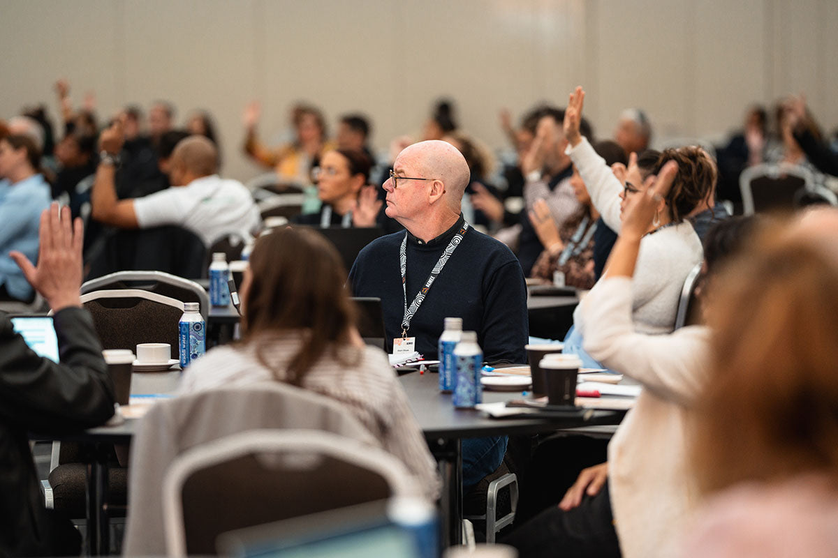 Audience delegates sitting at conference tables raising their hands to ask questions during an interactive panel discussion on community climate strategies.