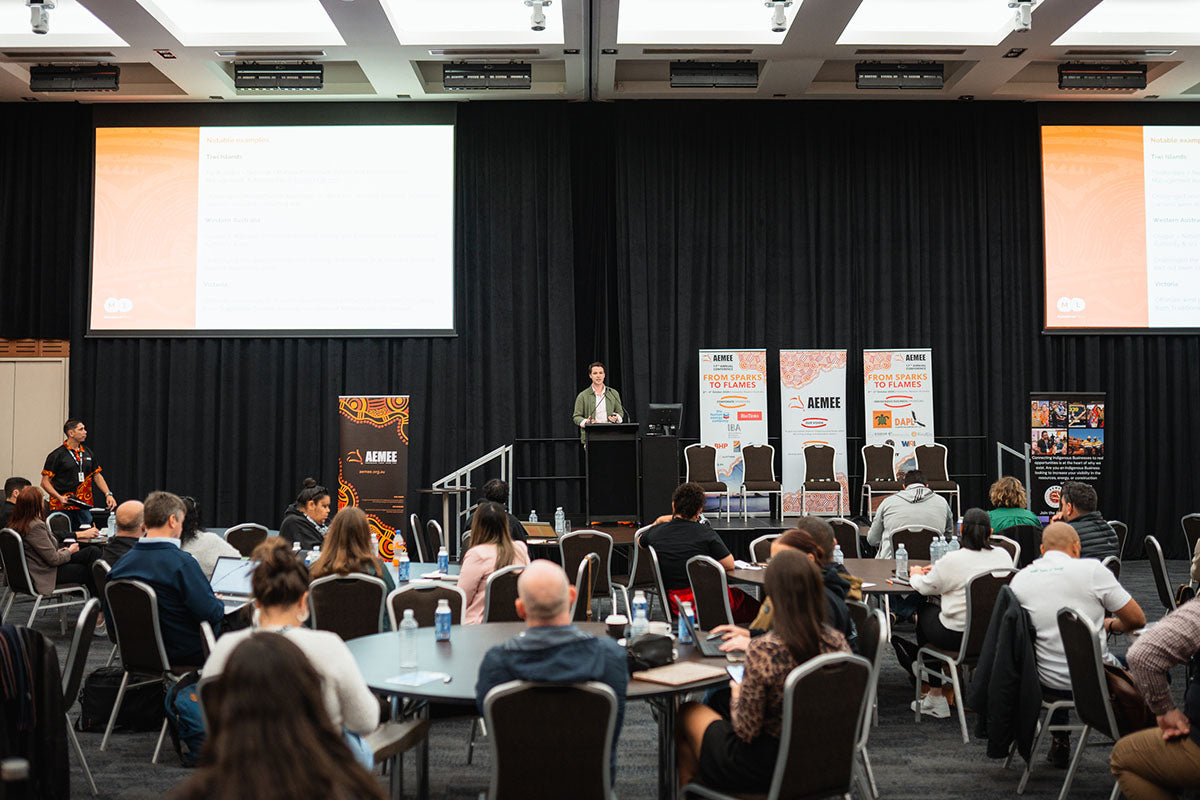 A wide view across rows of round tables filled with business professionals watching an industry breakout address inside the main auditorium layout.