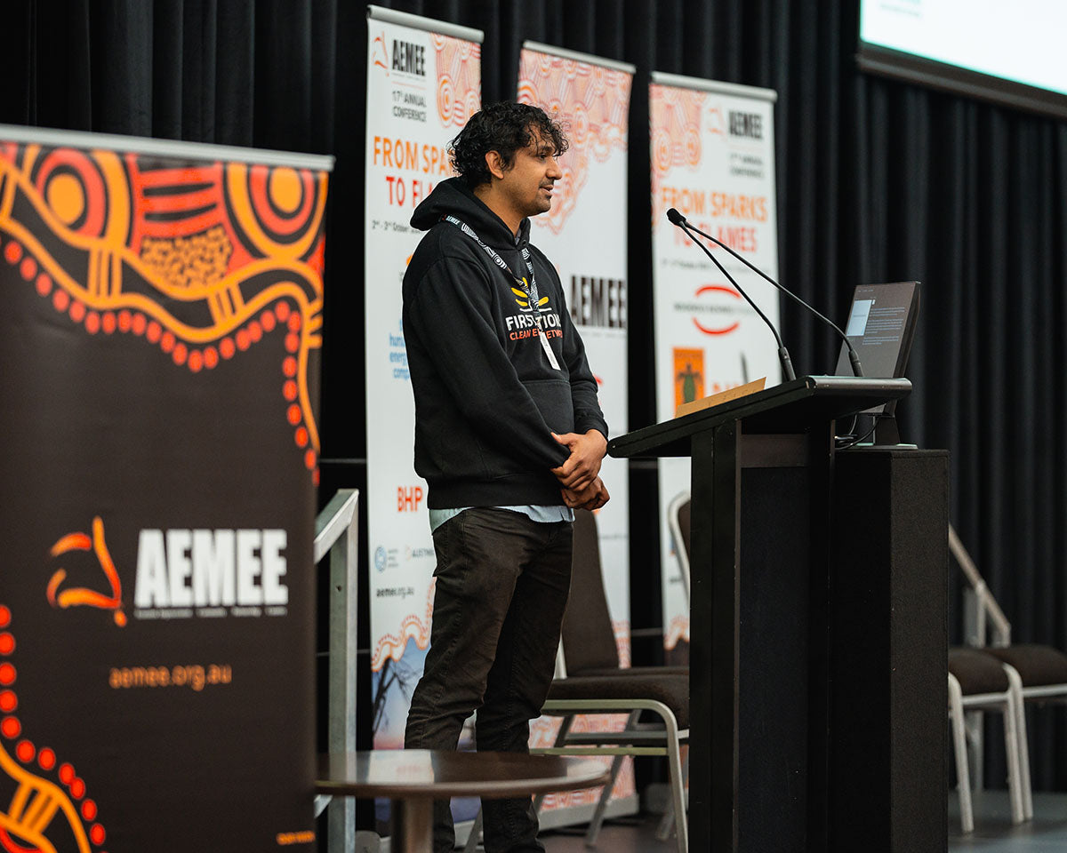 Kaneya Poudal standing at the stage microphone during a closing session block at the 17th Annual AEMEE conference.