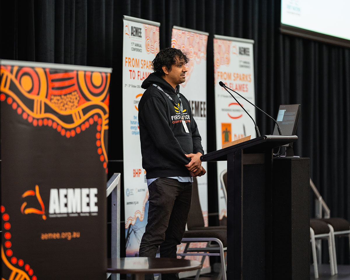 Kaneya Poudal of the First Nations Energy Network standing at the stage microphone, presenting on building business and supply chain opportunities in Australia's clean energy transition at the annual AEMEE conference.
