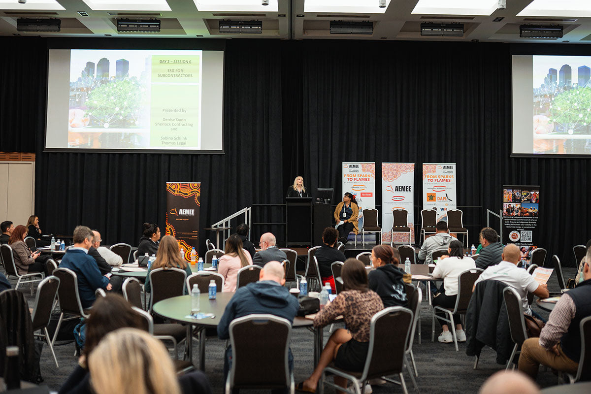 A wide viewpoint of seated conference delegates watching a breakout stream presentation beneath a large projector display inside the main hall auditorium layout.
