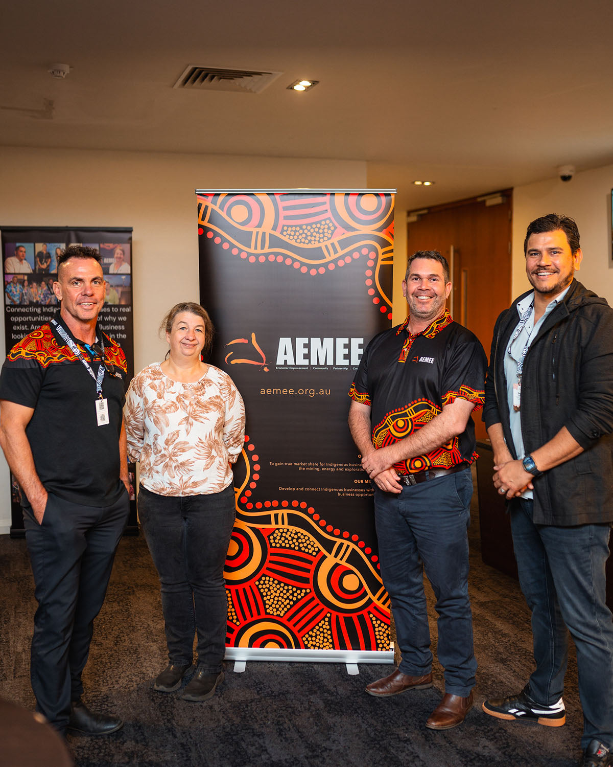 Chairperson Derek Flucker, a community delegate, CEO Jyi Lawton, and Director Raymond Pratt posing for a photo in front of a traditional First Nations graphic media banner.