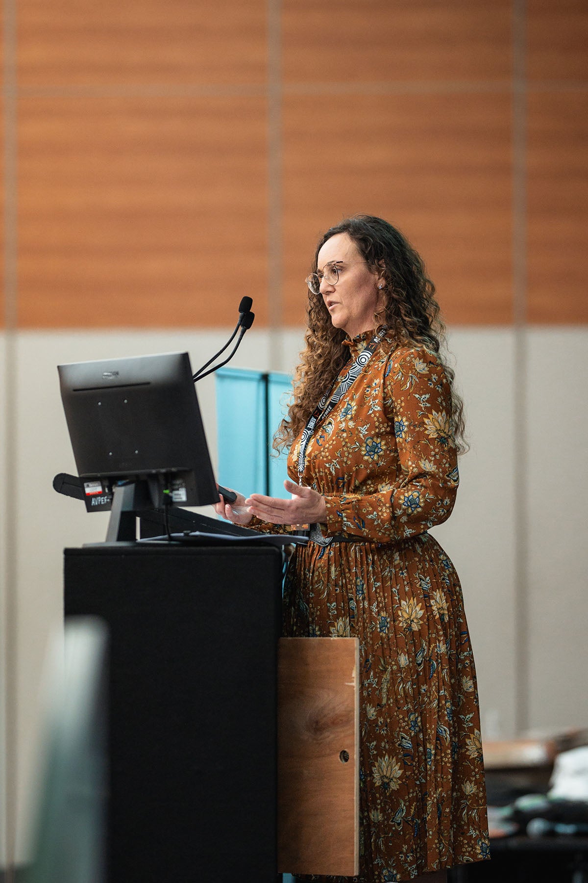 A female presenter with curly hair gesturing while addressing delegates from the microphone on commercial growth within the Indigenous business resources sector.