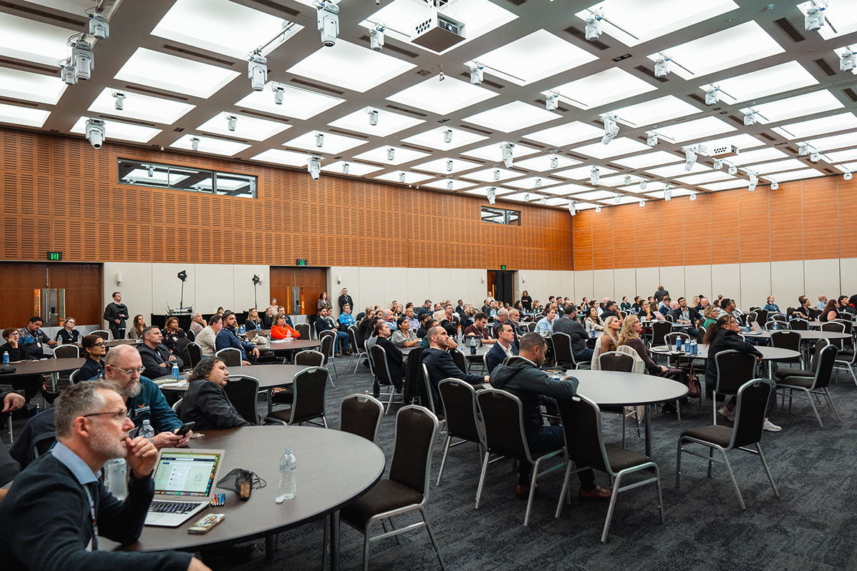 An expansive perspective of the packed main presentation hall with interactive roundtable setups during an industry forum at the AEMEE conference.