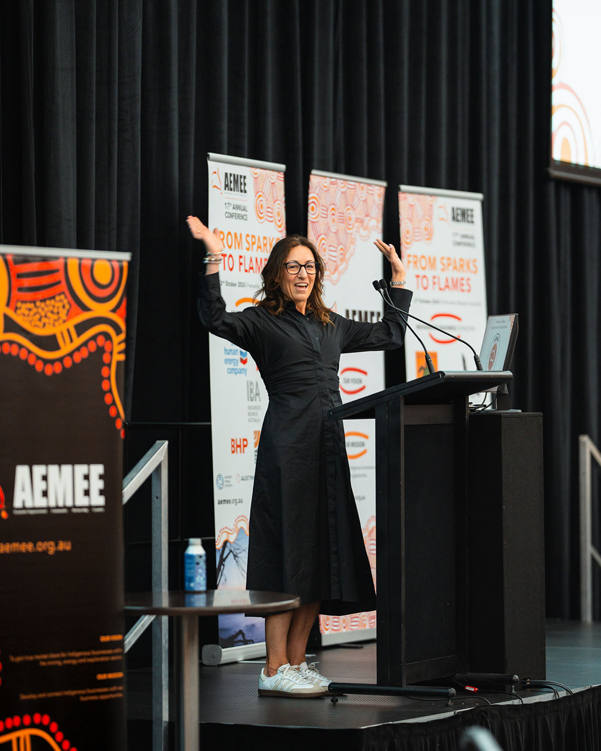 A female speaker gesturing with raised hands at the podium, delivering an impactful message on commercial pathways in the Indigenous business resources sector.