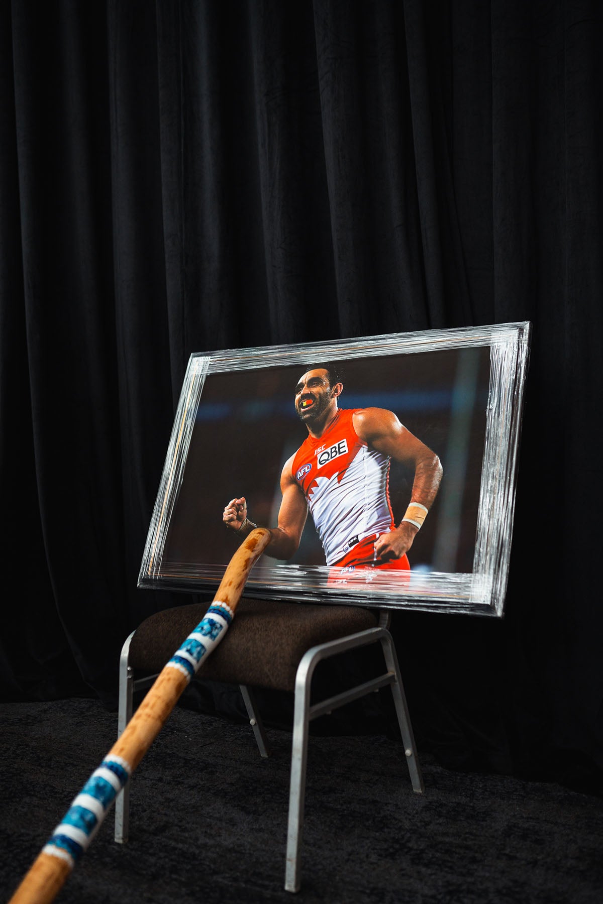 A framed, signed photograph of AFL player Adam Goodes on display next to a decorated message stick at a gala auction event supporting the Indigenous business resources sector.