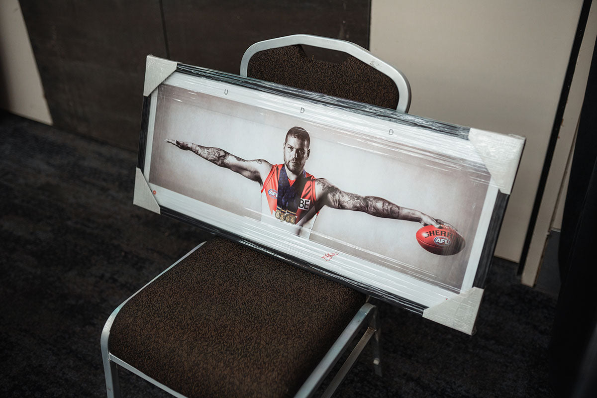 A large framed and wrapped panoramic photograph of legendary AFL player Lance Franklin displayed on a chair for a charity auction at the AEMEE conference.
