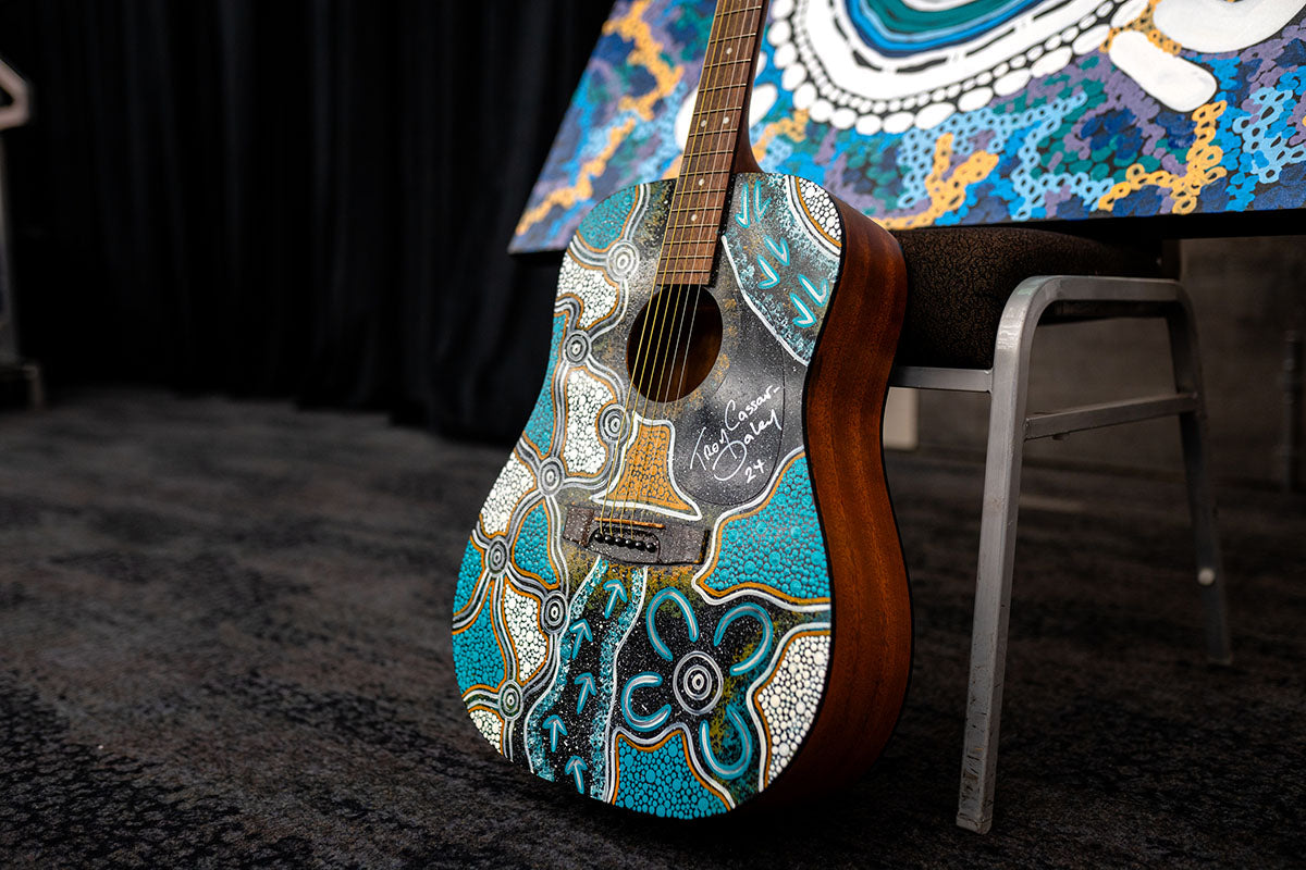 An acoustic guitar beautifully hand-painted with intricate blue, white, and teal traditional First Nations patterns, signed by the artist at the annual AEMEE conference.