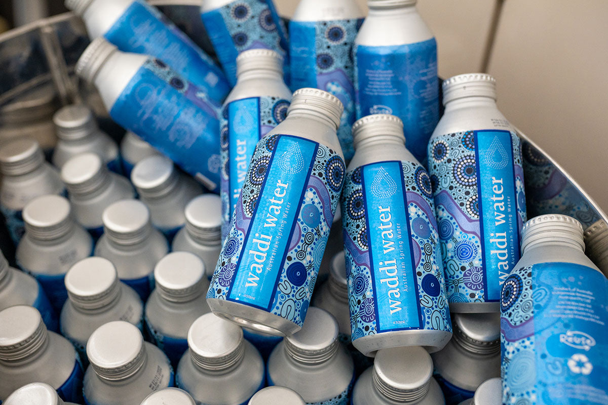A close-up view of aluminum water bottles decorated with traditional blue and white First Nations dot art patterns at the AEMEE conference.