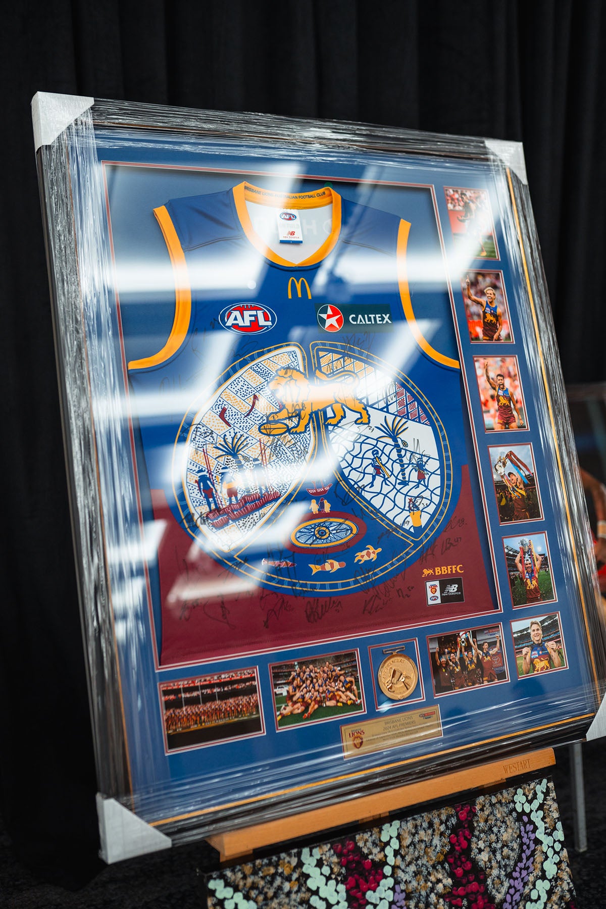 A framed AFL Guernsey from the Sir Doug Nicholls Indigenous Round, displaying custom artwork alongside Caltex and McDonald's branding at the AEMEE conference auction.