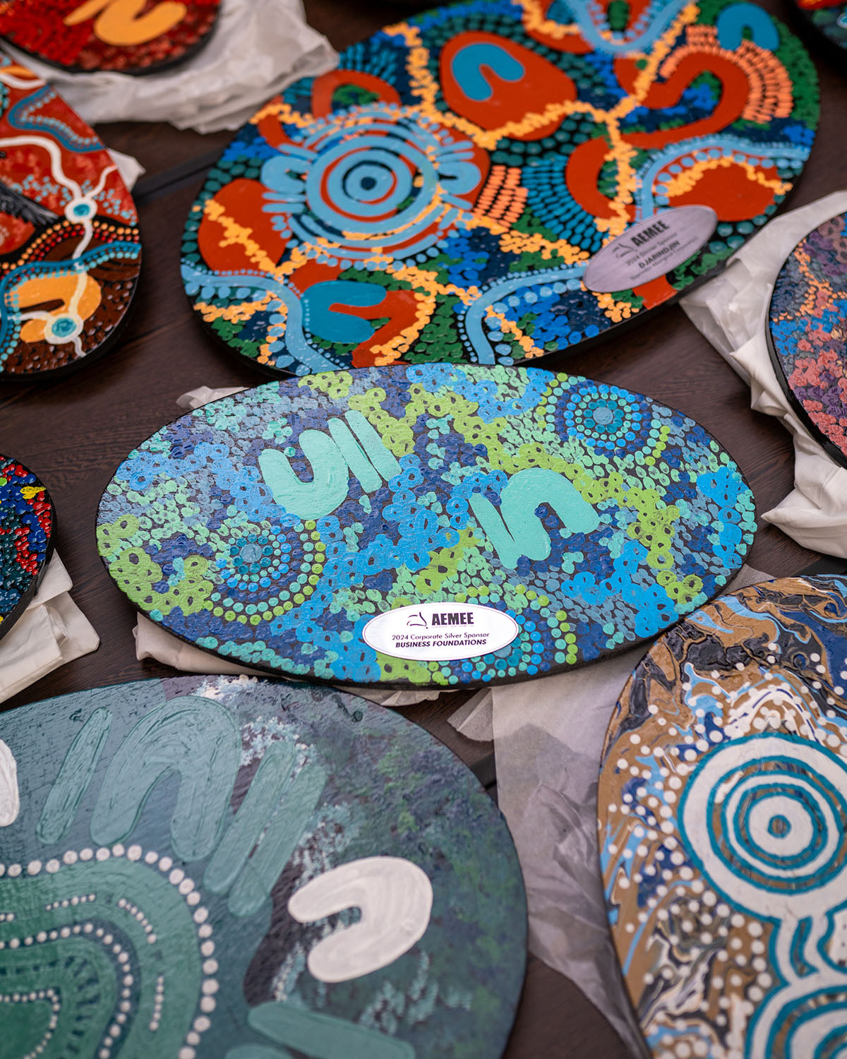 Beautifully vibrant, oval-shaped trophies featuring custom hand-painted traditional First Nations dot artwork, lined up on a presentation table for the winners.