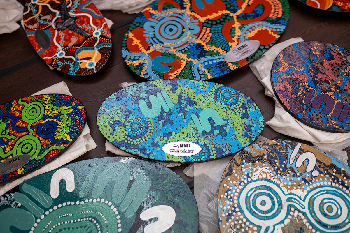 A close-up view of multiple custom-designed wooden plaques displaying unique Indigenous dreamtime paintings, ready to be presented at the 17th Annual AEMEE Awards