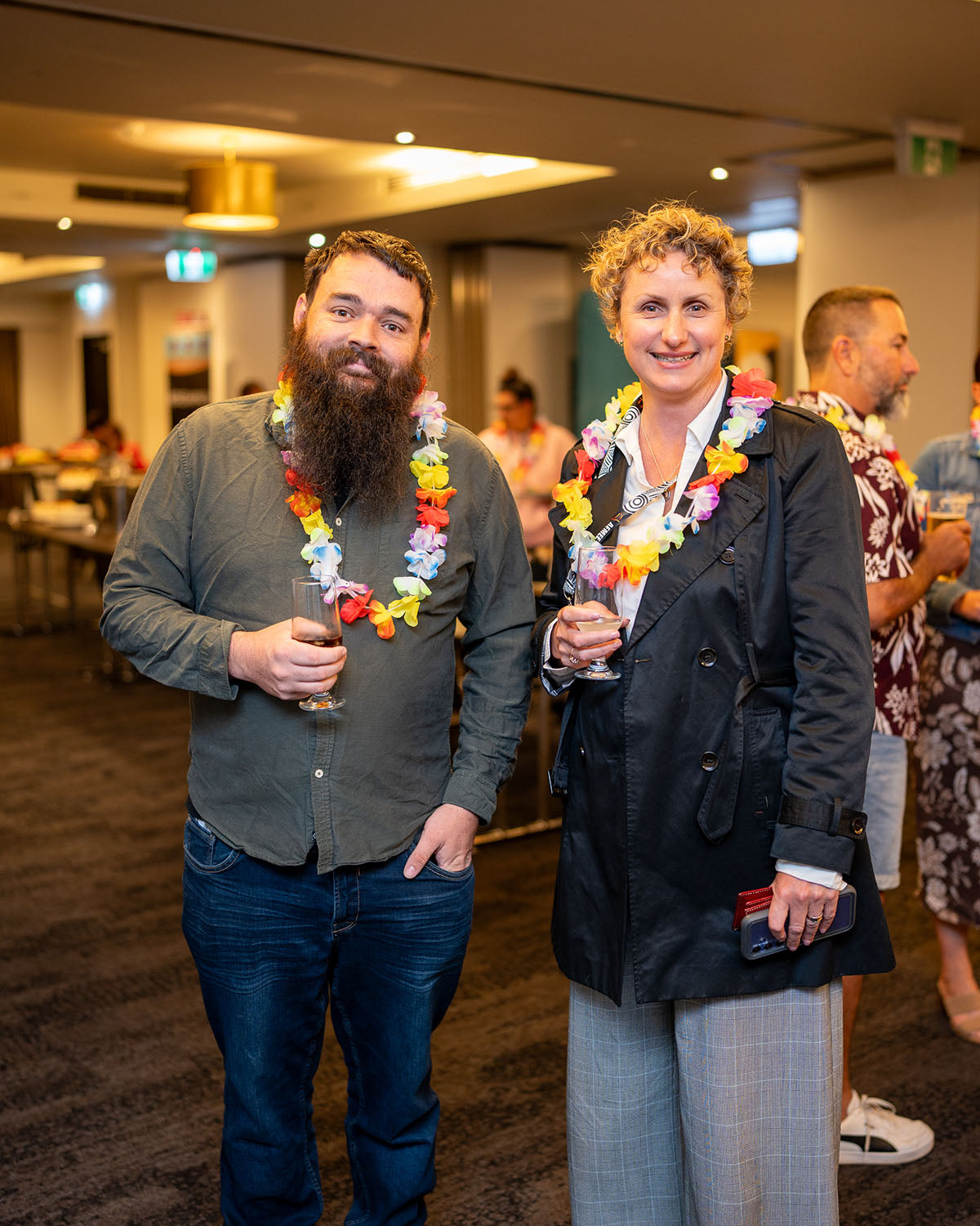 Portrait of a bearded businessman and his female corporate partner wearing festive flower garlands at the annual conference social event.