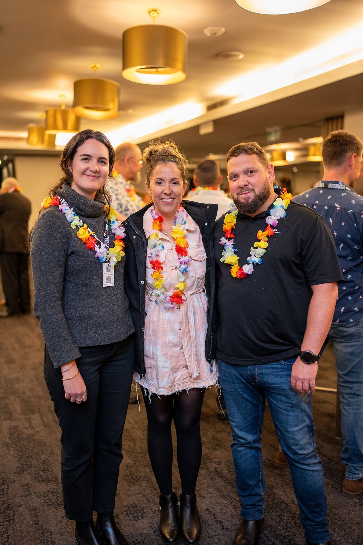 A close group shot of three conference attendees displaying their colorful floral lei garlands while socializing during the casual evening mixer.