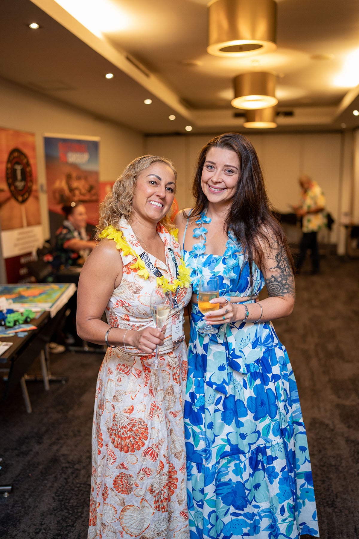 Two female entrepreneurs wearing bright yellow and blue themed floral patterns smiling during a breakout social networking hour.