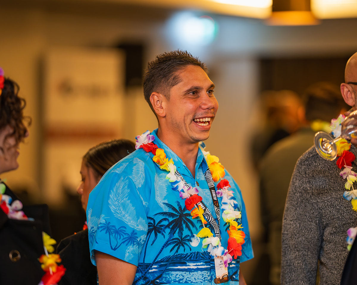 AEMEE CEO Jyi Lawton smiling warmly in a bright blue tropical Hawaiian shirt and colourful flower lei during the conference networking night