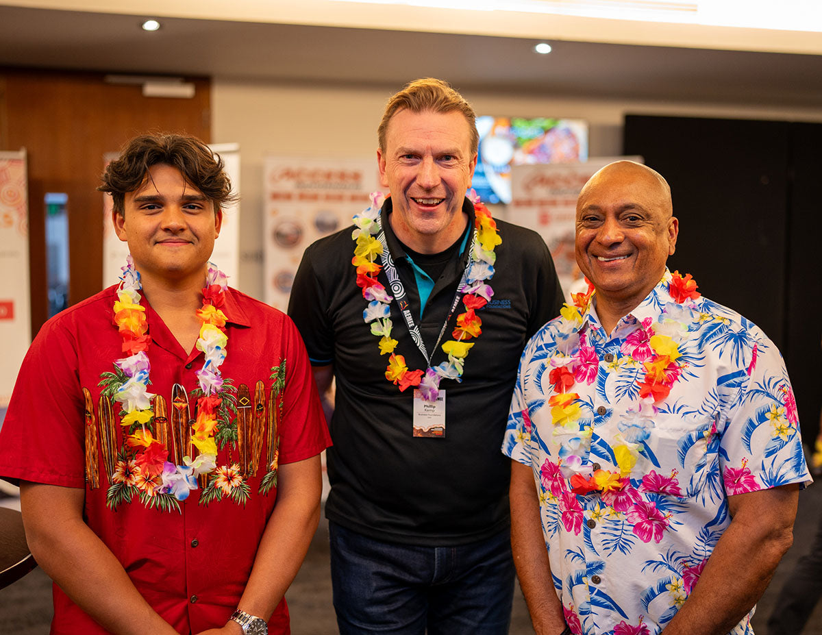 Three male conference attendees posing together while wearing festive flower leis, featuring bright tropical patterned shirts, at the evening business mixer.