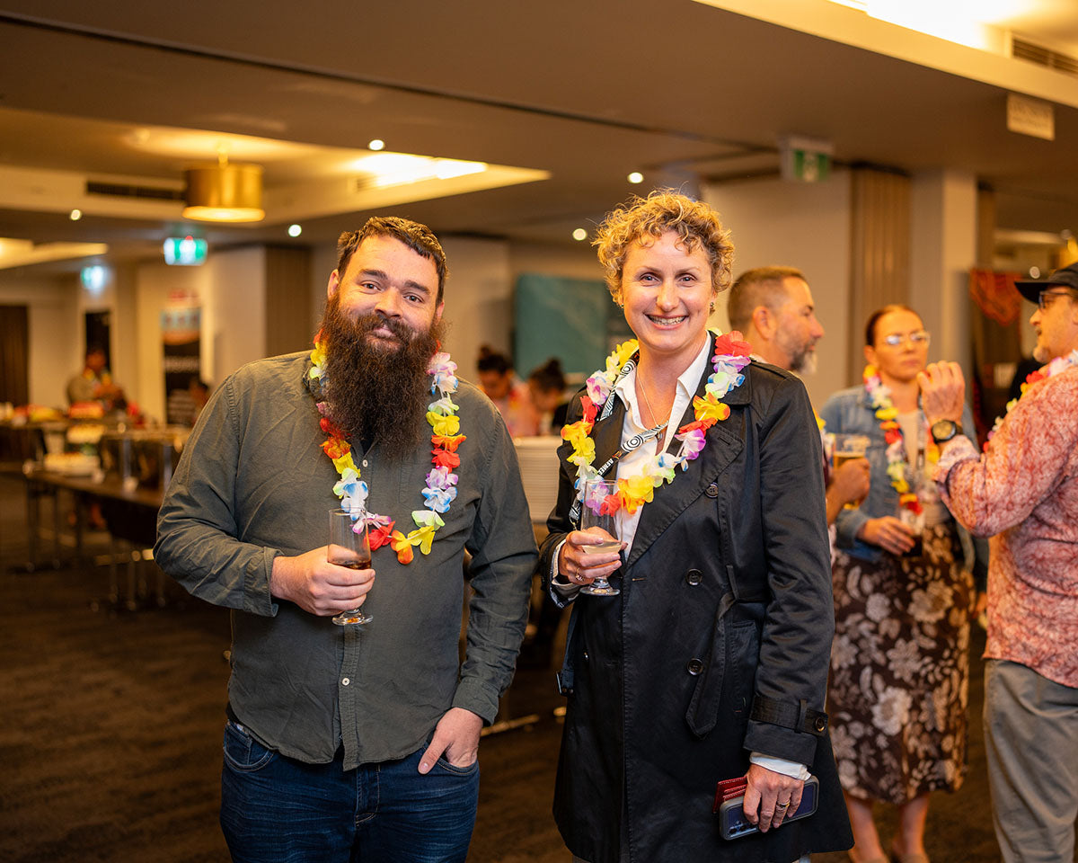 Two industry professionals wearing colorful lei garlands smiling together inside the venue during a casual B2B networking mixer.