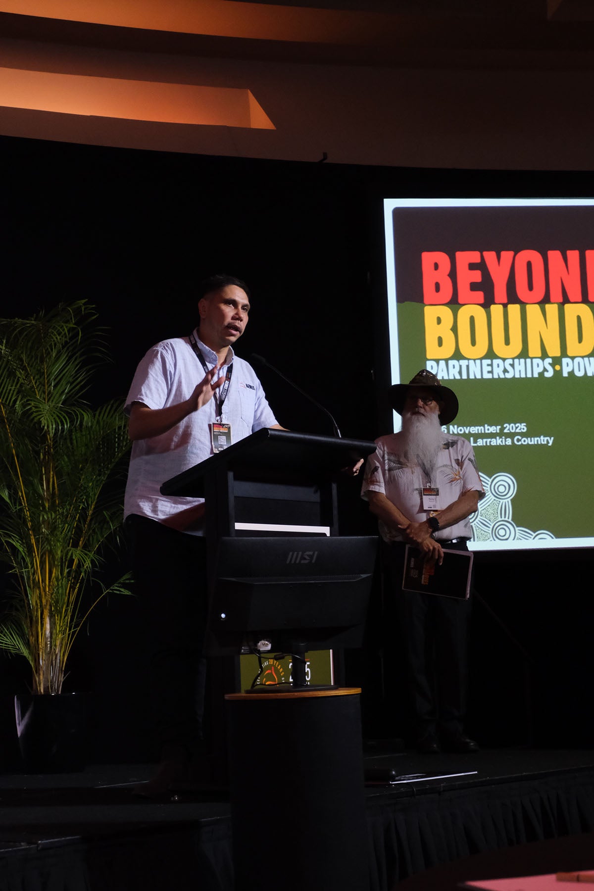 CEO Jyi Lawton, addressing delegates at the AEMEE conference with another presenter standing beside the podium.
