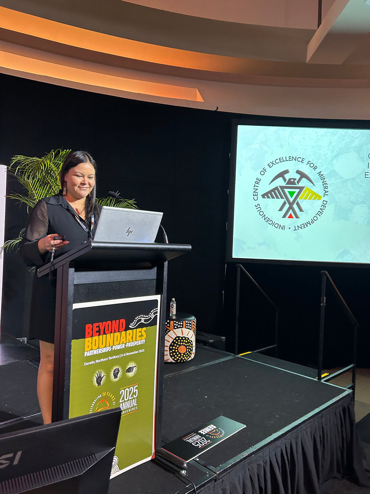 Speaker presenting at the AEMEE conference beside a Centre of Excellence for Aboriginal Economic Empowerment slide.