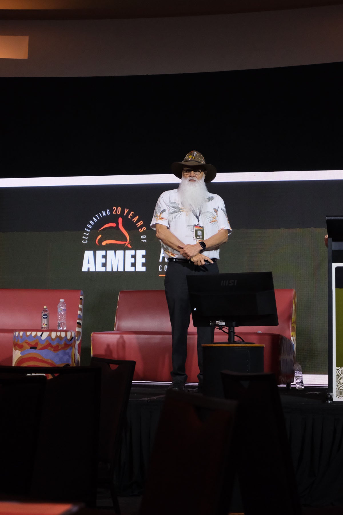 Speaker standing on stage at the AEMEE 2025 Annual Conference with event branding displayed behind him.