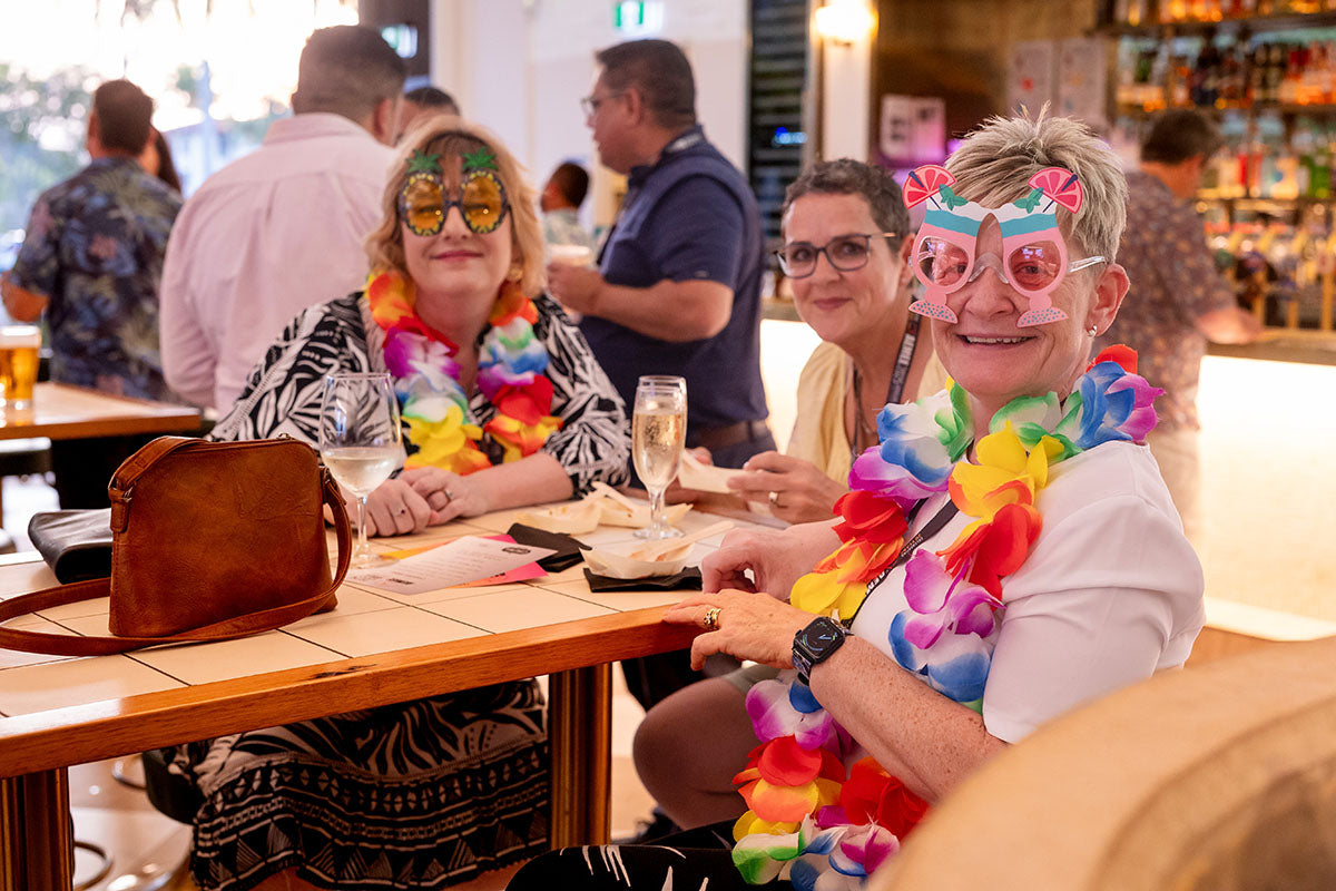 Delegates enjoying the AEMEE 2025 Annual Conference networking night in Darwin, wearing Hawaiian leis and novelty glasses