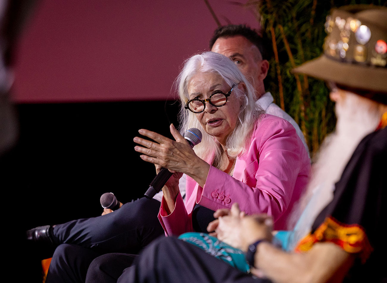 Professor Marcia Langton AO delivering a powerful keynote address from a dark-rust corporate podium, focusing on federal procurement standards and Indigenous capital.