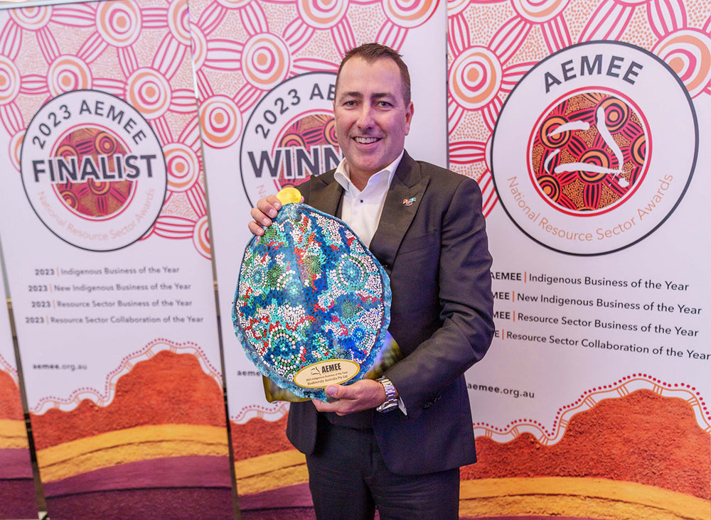 An executive partner holding a vibrant blue and green traditional shield trophy celebrating Biodiversity Australia as the Indigenous Business of the Year at the AEMEE conference.