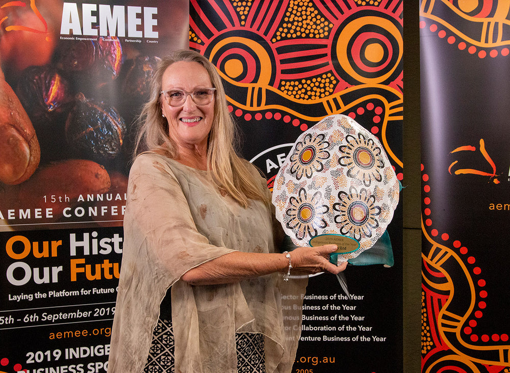 An executive leader holding a circular dot-patterned trophy celebrating Brida Pty Ltd as the 2019 Indigenous Business of the Year during an AEMEE conference evening presentation.