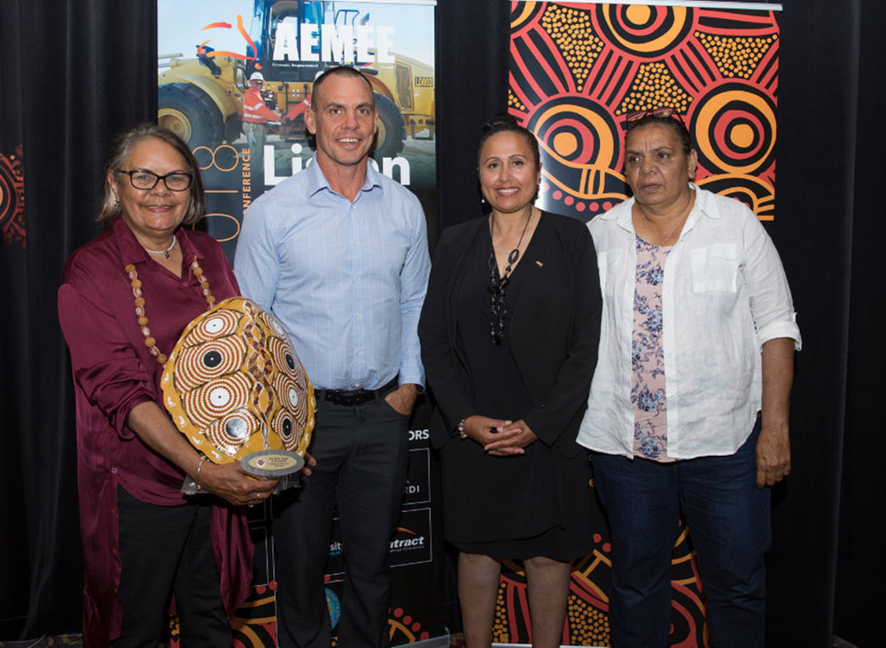 Regional business executives standing together on stage holding a gold and white patterned shield trophy awarded to Far West Coast Investments at the national AEMEE conference.