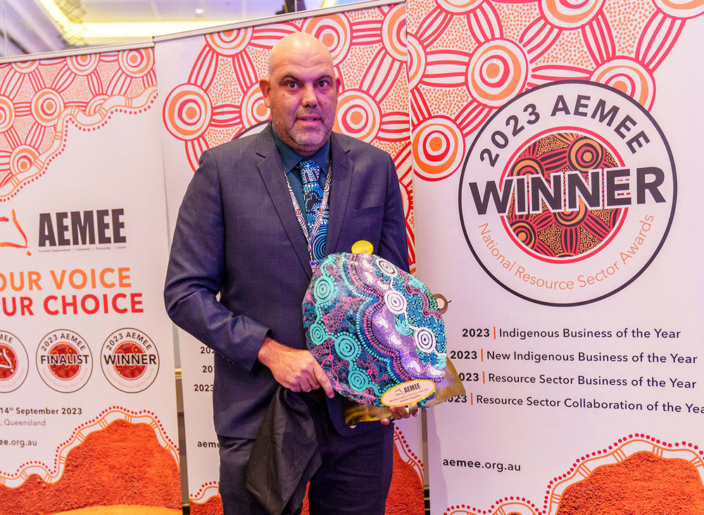 A corporate delegate in a suit holding a custom shield trophy awarded to Gawun as the New Indigenous Business of the Year within the AEMEE conference network.
