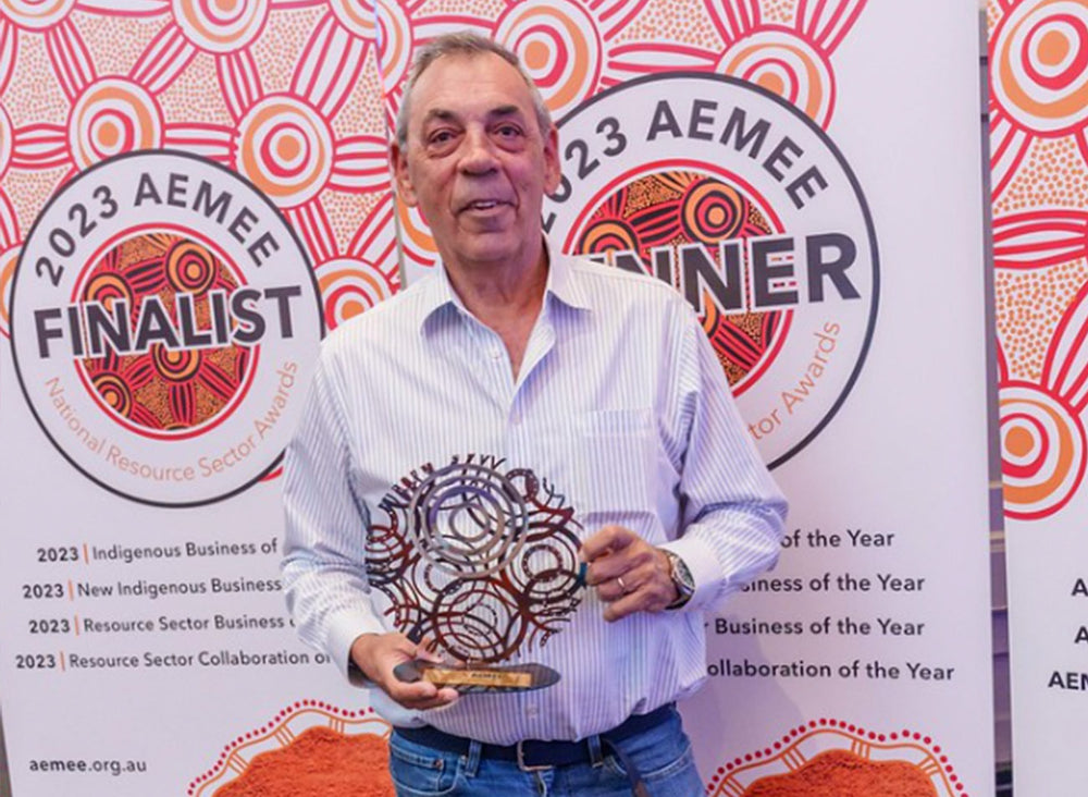 John Briggs holding an intricate metallic trophy element in front of an official media banner backdrop at the annual AEMEE conference awards ceremony.