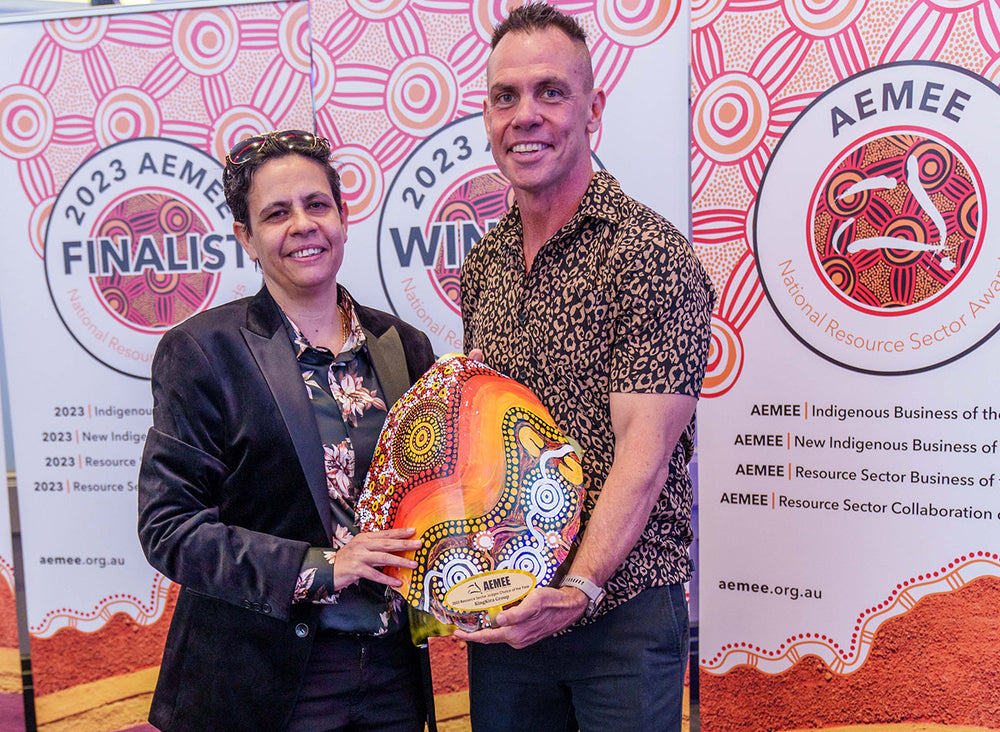 Two business partners smiling and holding an ochre-toned traditional shield trophy together for the Judges Choice category at the national AEMEE conference awards.