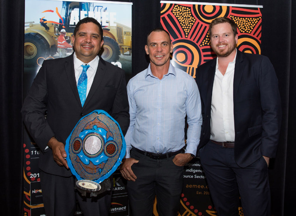Three business directors standing on stage holding a unique carved shield trophy celebrating Moec Pty Ltd as the 2018 New Indigenous Business of the Year at the AEMEE conference.