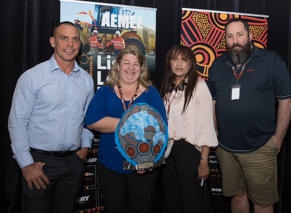 Corporate team members standing together on stage holding a blue hand-painted shield trophy for the 2018 Resource Sector Business of the Year category at an AEMEE conference.