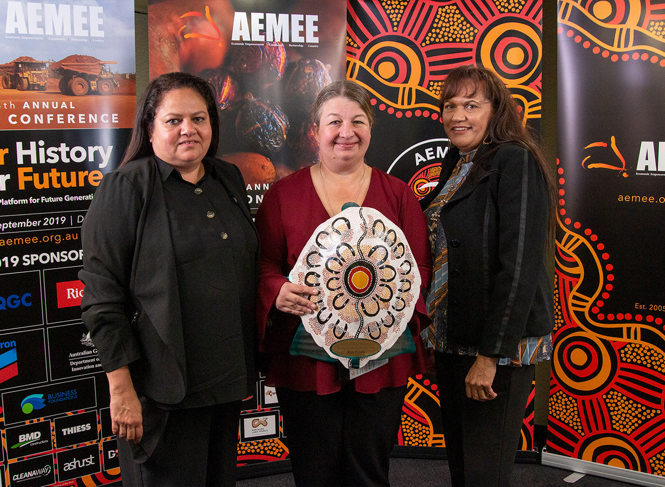 Three corporate representatives holding a white shield trophy with concentric line designs for the 2019 Resource Sector Business of the Year category at the AEMEE conference.