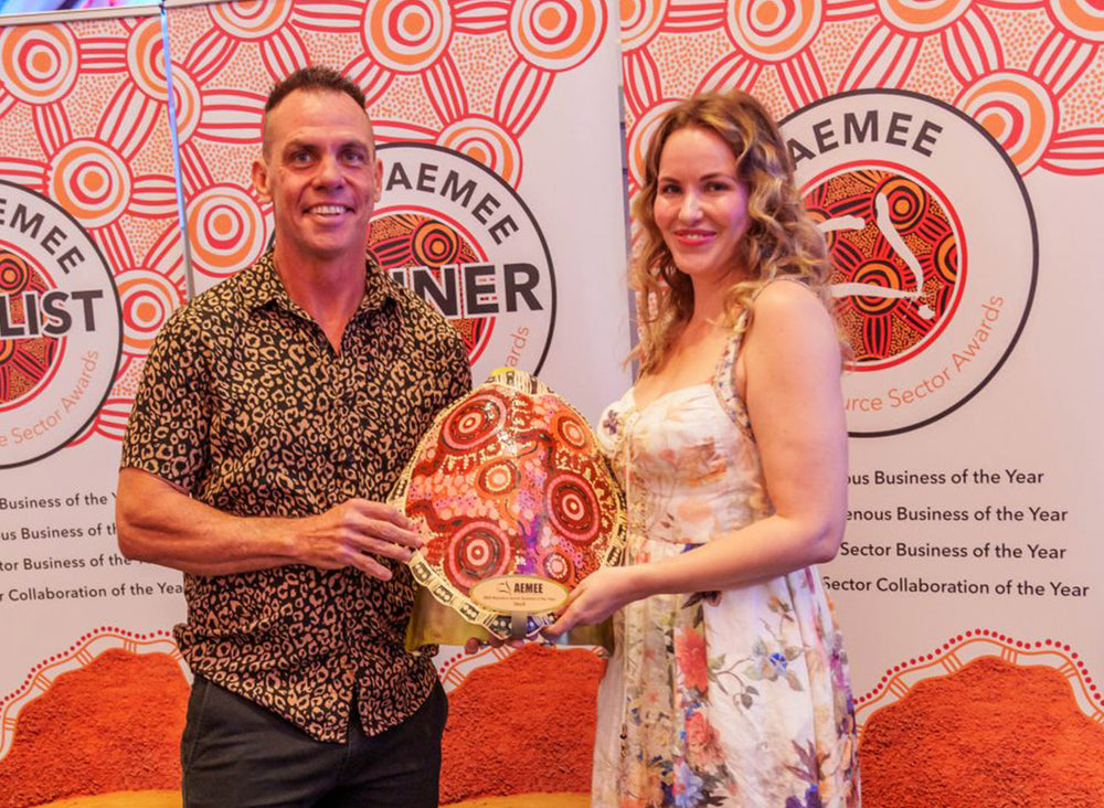 A corporate representative holding a large hand-painted traditional shield trophy awarded to Shell as the Resource Sector Business of the Year at the AEMEE conference.