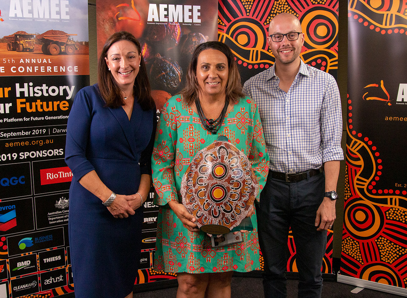 Business partners posing together with a traditional artwork shield trophy celebrating Waayni Downer Joint Venture as the Joint Venture Business of the Year at an AEMEE conference.