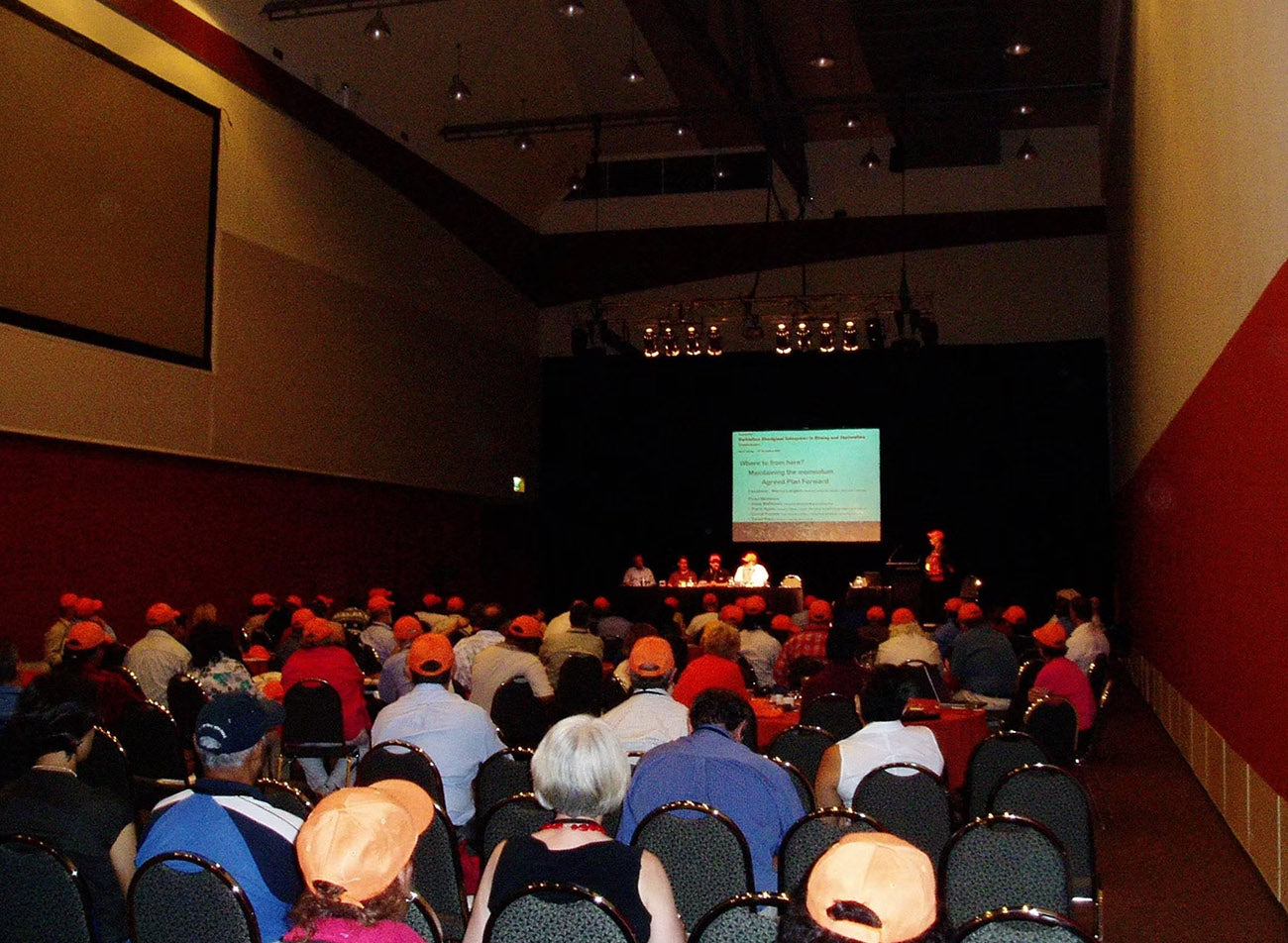 An auditorium filled with seated delegates wearing matching orange caps during a plenary session panel at the inaugural AEMEE conference in Alice Springs.