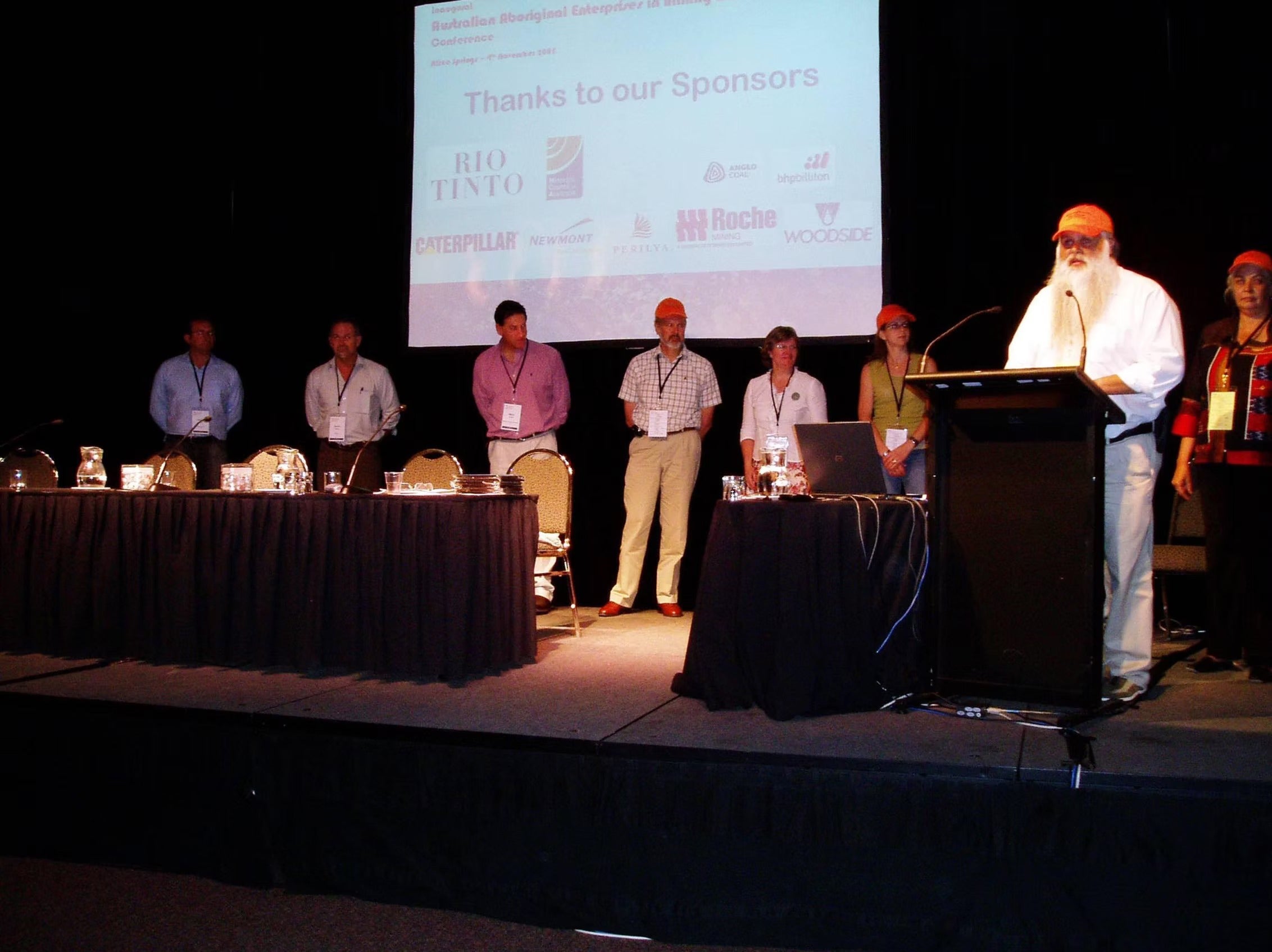 Historical photo from the inaugural AEMEE conference in 2005, showing Indigenous leaders on stage with major industry sponsors including Rio Tinto and BHP.